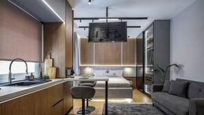 Eine moderne Küche mit integriertem Mikrowellenherd, einem Essbereich mit Tisch und Stühlen, einer Couch und einem an der Wand montierten Fernseher.