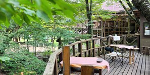 A wooden deck with tables and chairs, surrounded by trees and a wooden structure in the background. - kasibessou guranpingu himesyara  (Kirishima)
