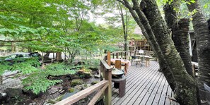 Um deck de madeira com um pequeno lago, rodeado por árvores e uma estrutura de recreação de madeira.
