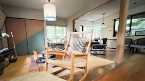 Ein modernes Wohnzimmer mit einem Holzschaukelstuhl, einem Couchtisch und einem großen Fenster mit Blick ins Freie.