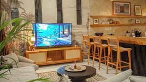 Olohuone, jossa on televisio, sohva, sohvapöytä ja baaritiski jakkaroineen.