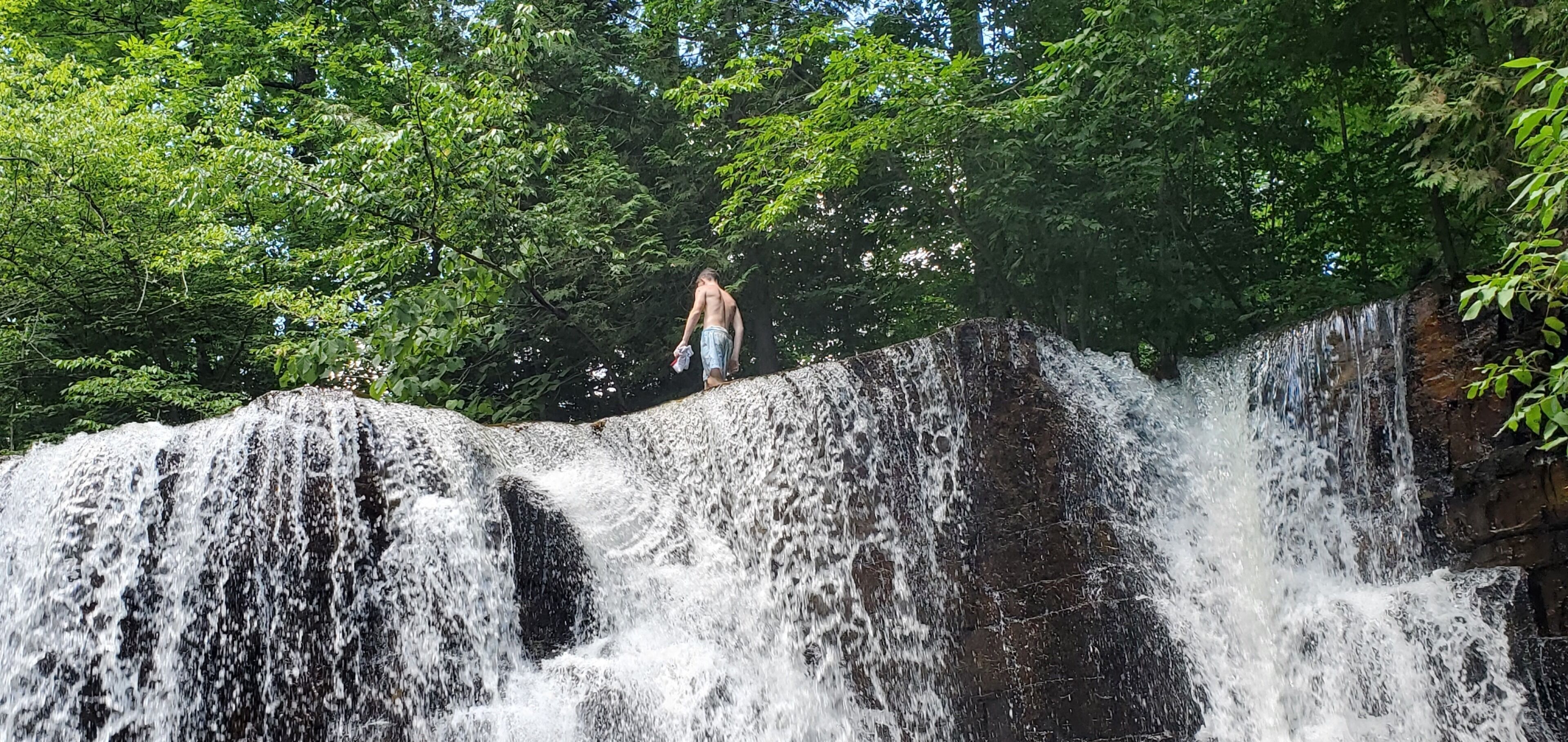 Una cascada con una persona de pie sobre un saliente rocoso.