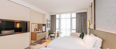 A hotel room with a large bed, a desk with a chair, a TV, and a window with curtains.