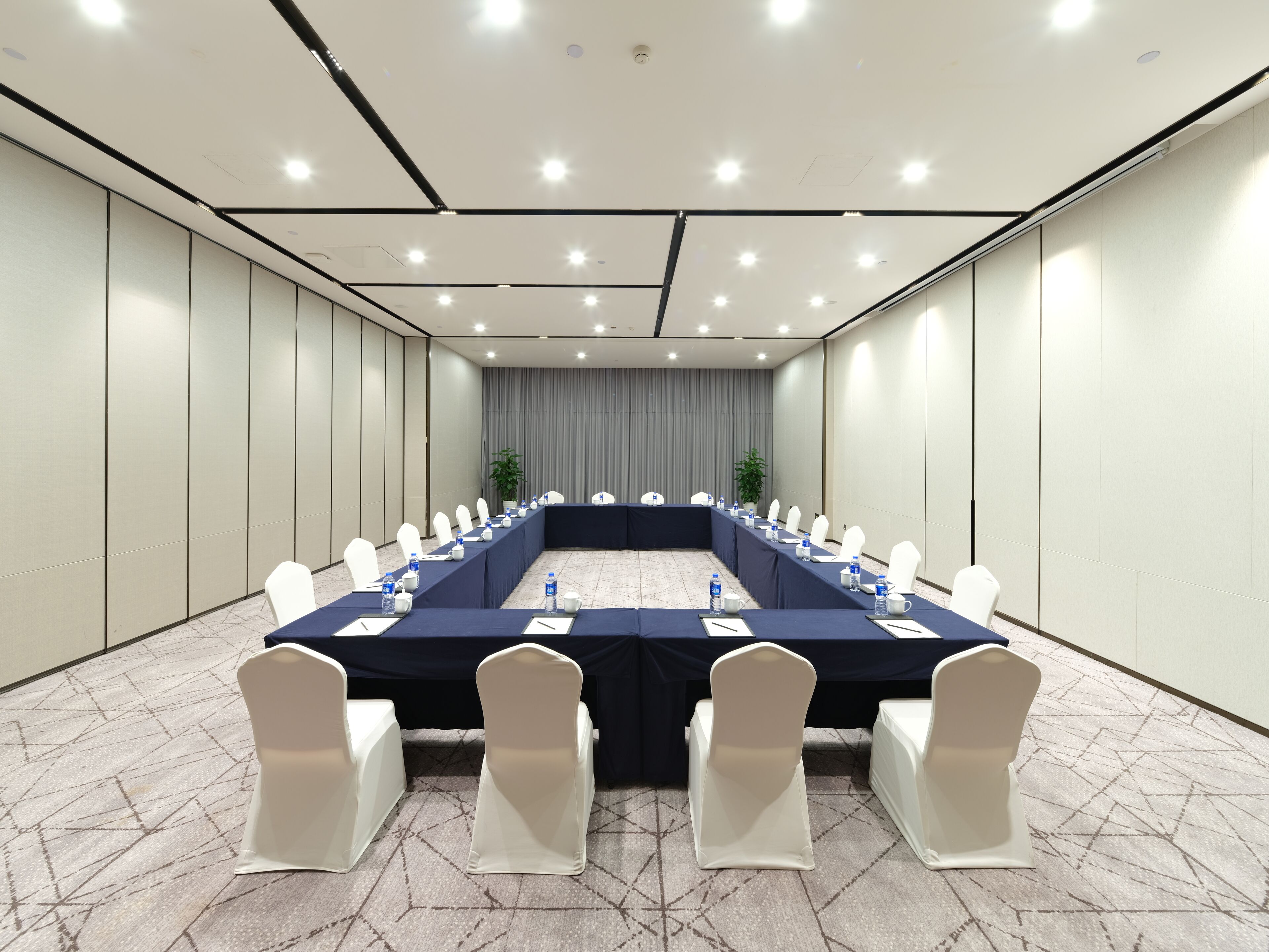 A conference room with a long table, white chairs, and a dark blue tablecloth.