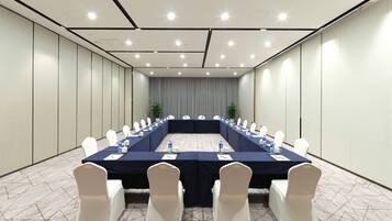 Un salón de conferencias con una larga mesa, sillas blancas y un mantel azul oscuro.