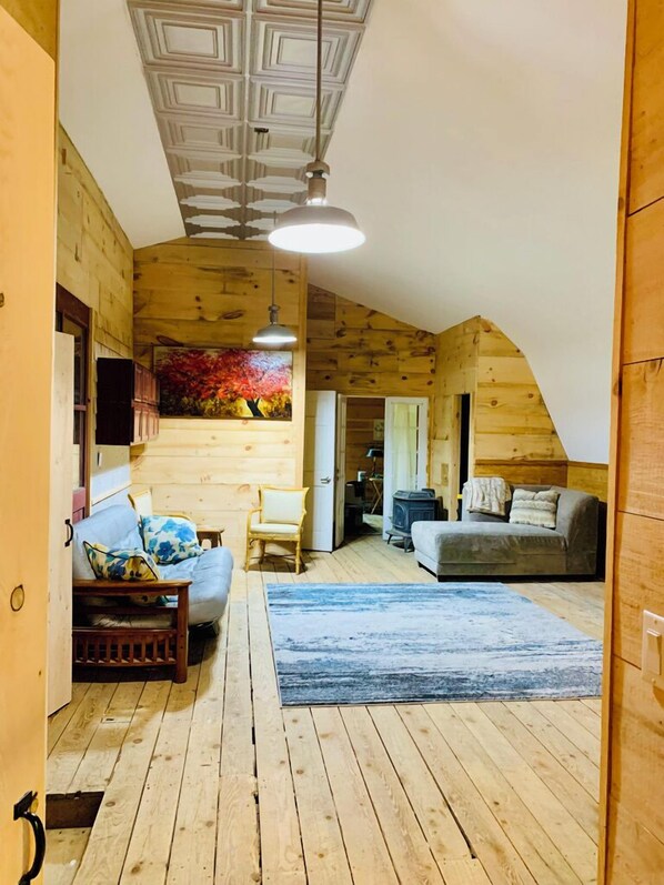 En mysig stuga med träpanel på väggarna, en soffa, en fåtölj och en öppen spis.