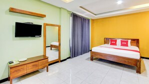 Une chambre d’hôtel avec un lit, une télévision, un miroir, une commode en bois et une fenêtre avec des rideaux.