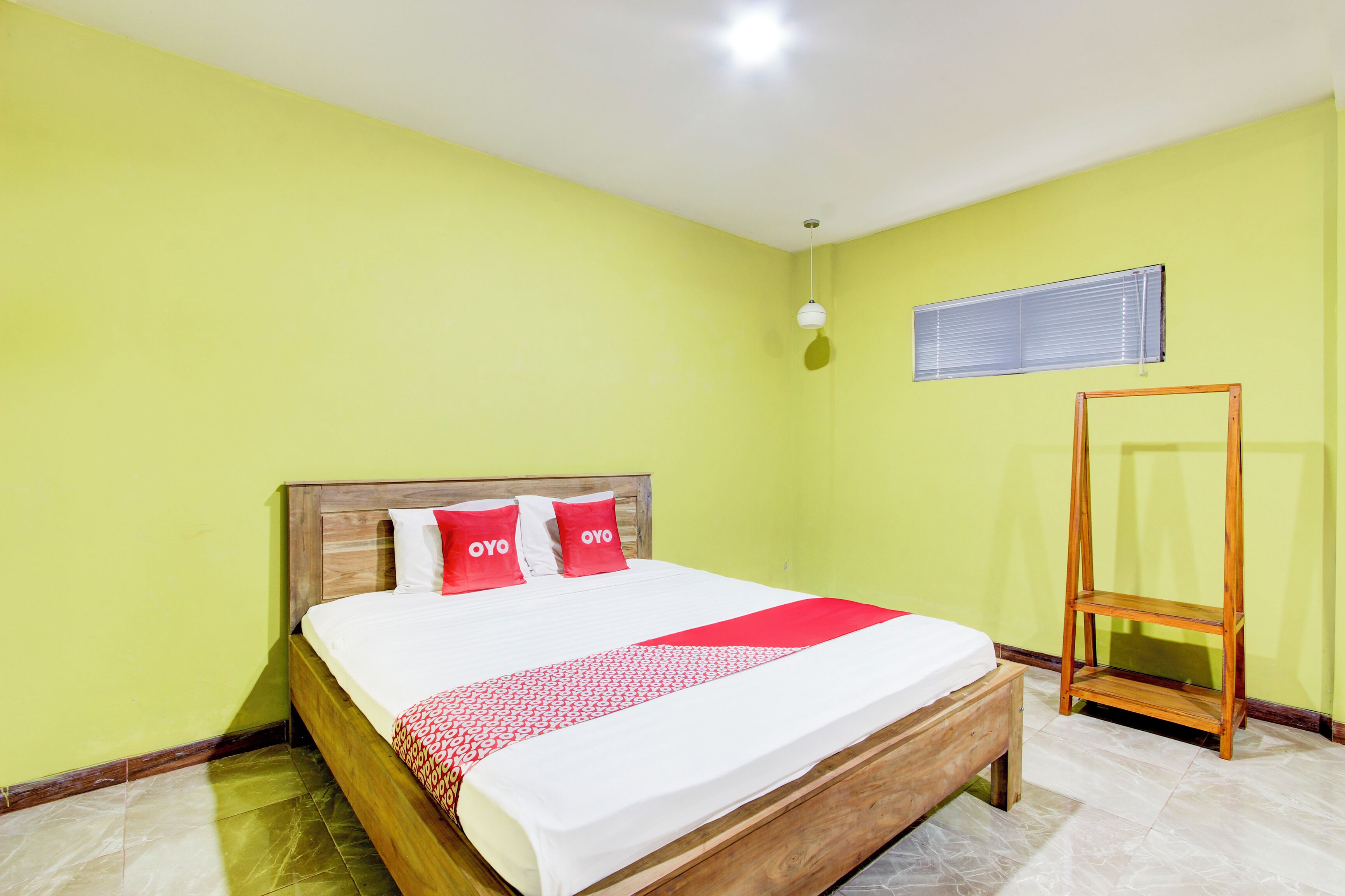Una habitación con una cama, cabecera de madera, colcha roja y blanca, y una estantería de madera.