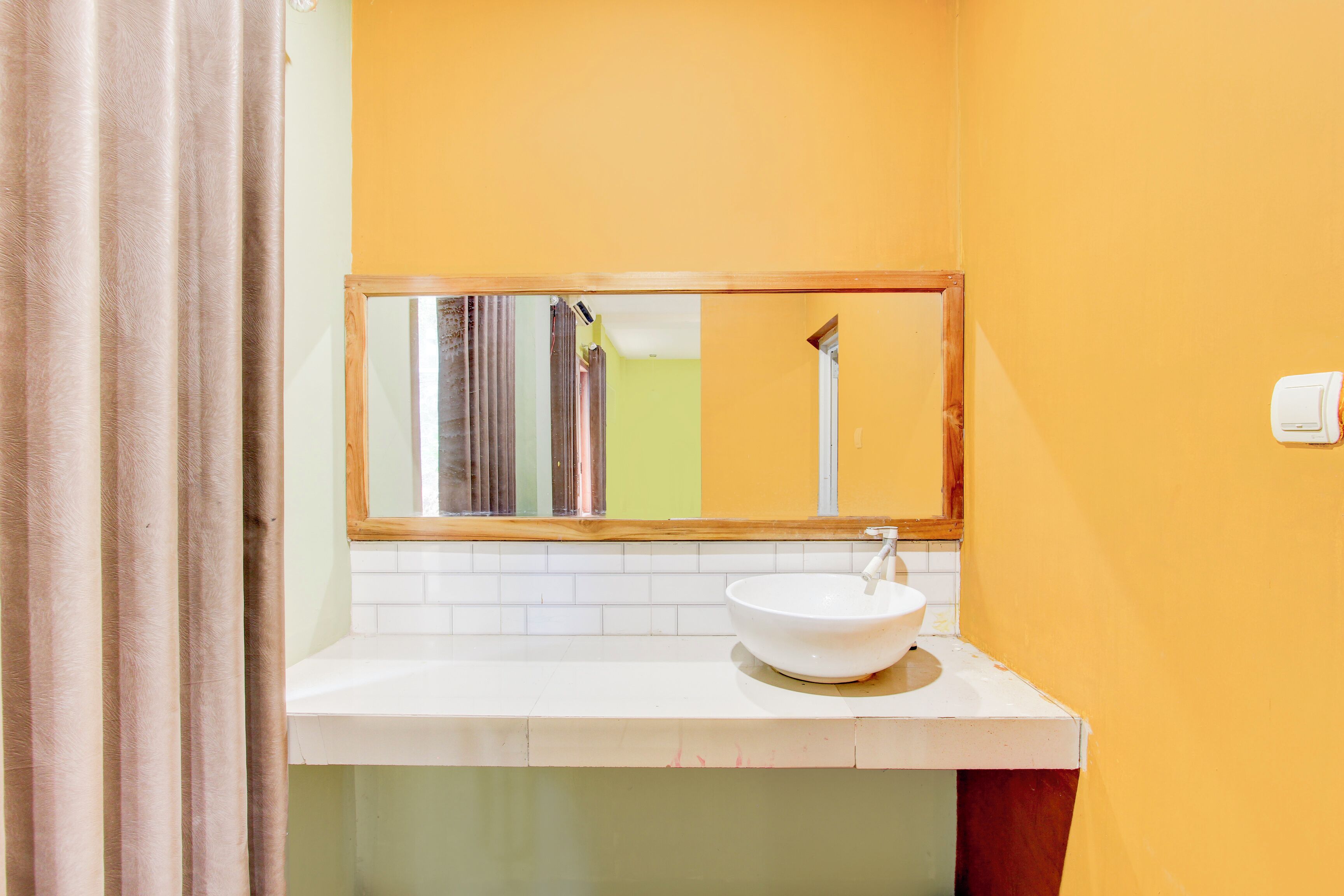 Un baño con un lavabo blanco, un espejo y una pared amarilla.