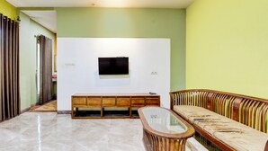 Un salon spacieux avec un téléviseur à écran plat fixé à un mur blanc, un banc en bois avec espace de rangement et une table basse en verre.