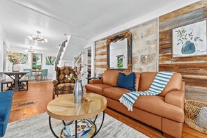 Uma sala de estar com um sofá de couro marrom, uma mesa de centro redonda de madeira e um espelho grande numa parede de pedra.