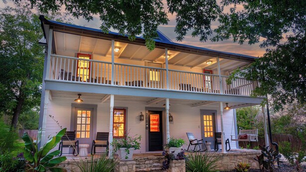A two-story house with a porch, outdoor seating, and a stone pathway leading to the entrance.