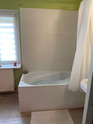 Een badkamer met een bad, een raam met zonwering en een radiator.