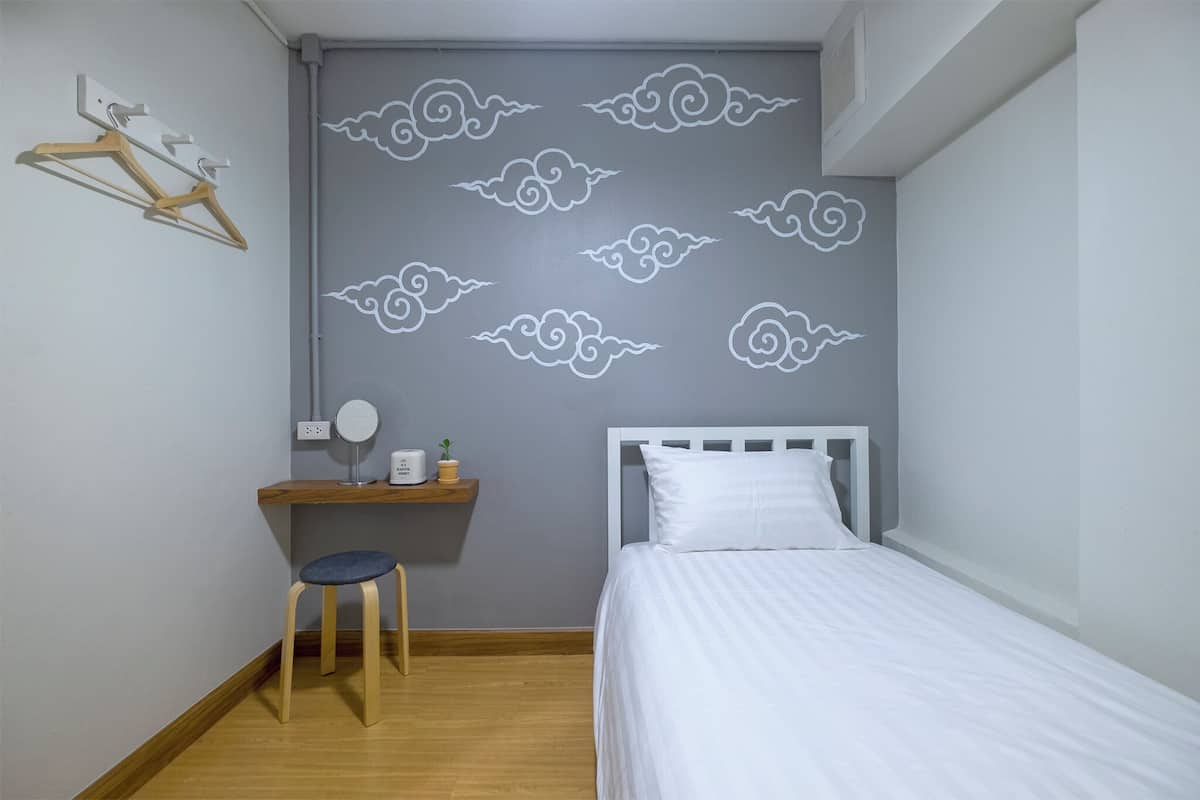A bedroom with a bed, a desk with a chair, a wall-mounted shelf, and a wall decoration of clouds.