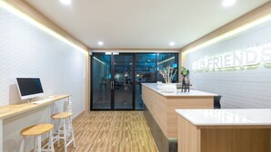 A reception area with a wooden desk, two white bar stools, a computer, and a wall with the text "RED FRIENDS". - BED Friends Poshtel (Chiang Rai)