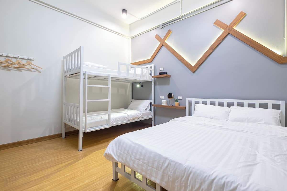 A bedroom with a bunk bed, a single bed, a wooden cross decoration, and a shelf with a lamp and a small plant.