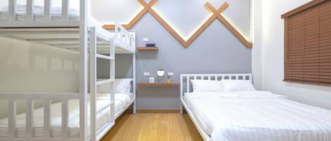 A room with bunk beds, a bedside table with a lamp, and a wall-mounted shelf.