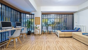 A modern living room with a wooden floor, two grey chairs, a sofa with blue cushions, a small table with a plant, and a TV on a desk. - BED Friends Poshtel (Chiang Rai)
