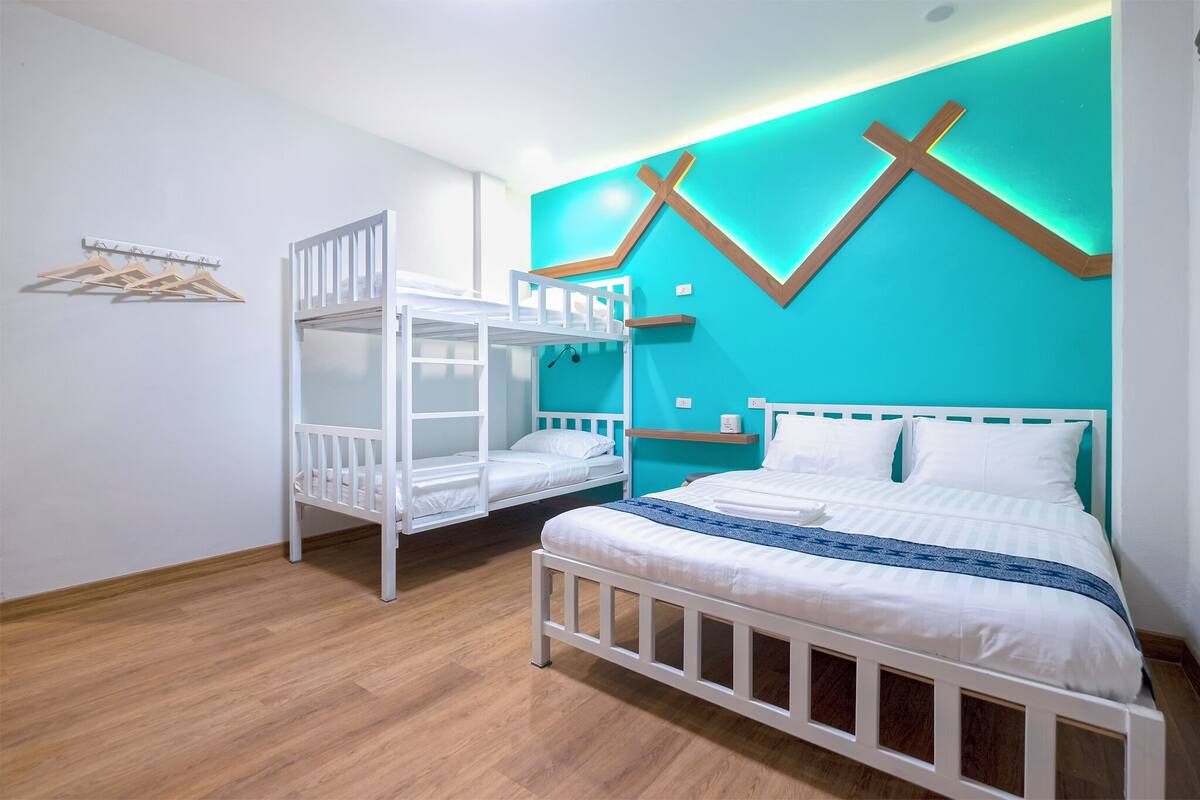 A room with a bunk bed, a single bed, wooden flooring, a wall-mounted cross, and a lighted wall design.