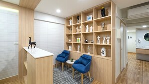 Un'accoglienza moderna con una scrivania in legno, due sedie blu e uno scaffale con diversi oggetti decorativi.