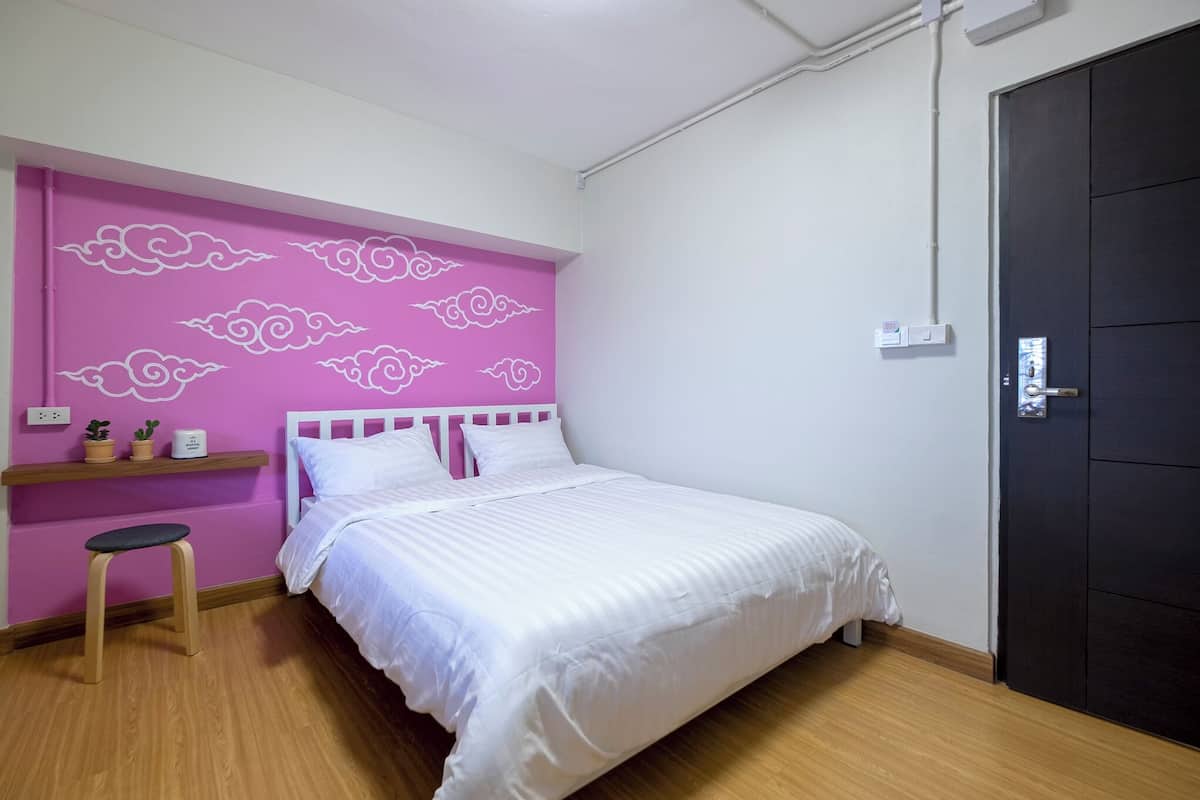A room with a bed, a stool, a shelf with decorative items, and a door.