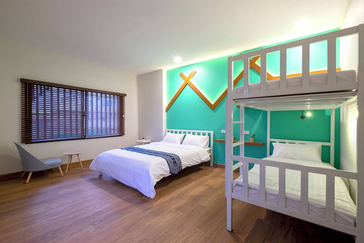 A modern bedroom with a bunk bed, a single bed, a desk, and a chair.