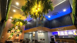 A restaurant with a modern interior, featuring hanging plants, wooden tables, and a counter with a sign reading "EAT". - BED Friends Poshtel (Chiang Rai)