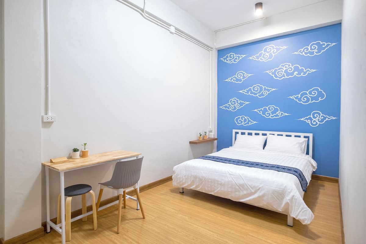 A bedroom with a bed, a desk, a chair, and a blue wall with cloud patterns.