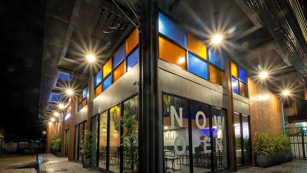 A modern building with large glass windows and a sign that reads "NOME." - BED Friends Poshtel (Chiang Rai)