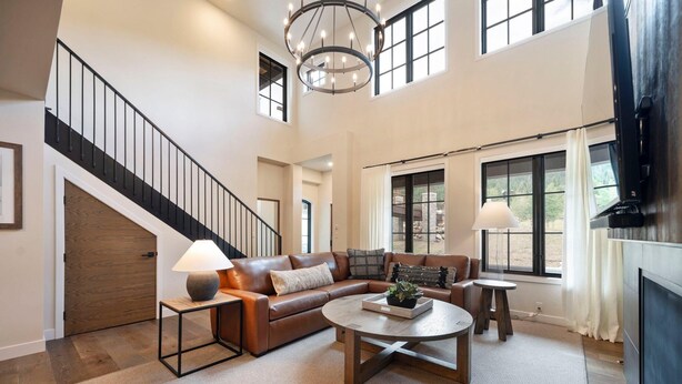 A spacious living room with a large sectional sofa, a coffee table, and a TV. A staircase with a black railing leads to an upper level. - Slopeside Retreat | Includes Two 1-Day Lift Tickets (Tamarack)