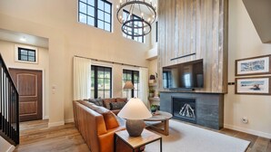 A spacious living room with a fireplace, a high ceiling, and a staircase leading to another level. - Slopeside Retreat | Includes Two 1-Day Lift Tickets (Tamarack)