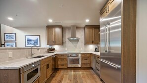 A modern kitchen with wooden cabinets, stainless steel appliances, and a tiled backsplash. - Slopeside Retreat | Includes Two 1-Day Lift Tickets (Tamarack)