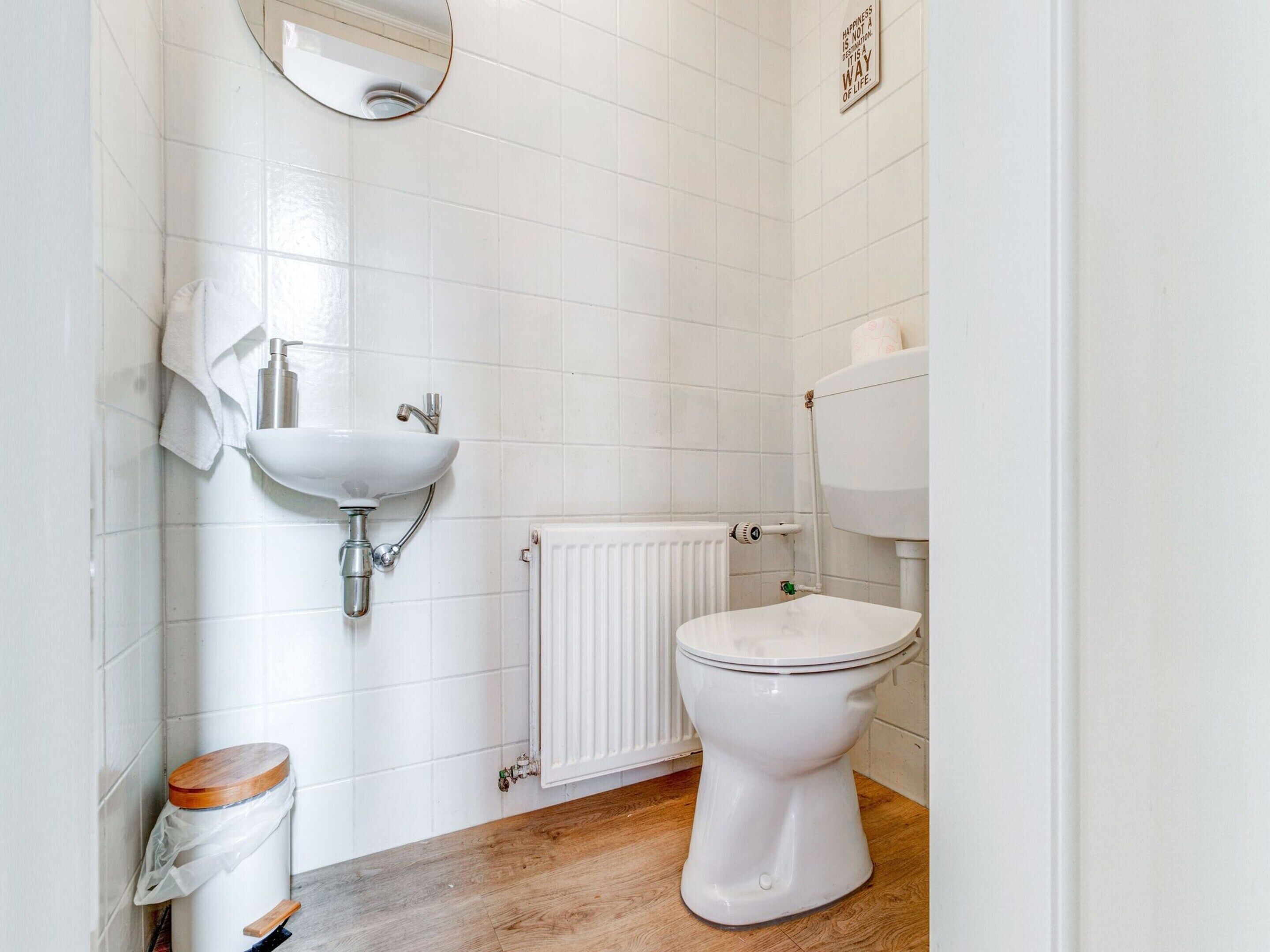 Une petite salle de bain propre, avec des carreaux blancs, un lavabo blanc, des toilettes et un plancher en bois.