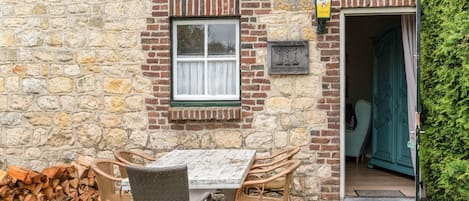 A stone building with a wooden table and chairs outside, a window, and a door leading inside.