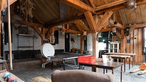 Ein rustikaler Holzraum mit einem Tischtennisschrank, einem weißen runden Tisch und einem Korbstuhl.