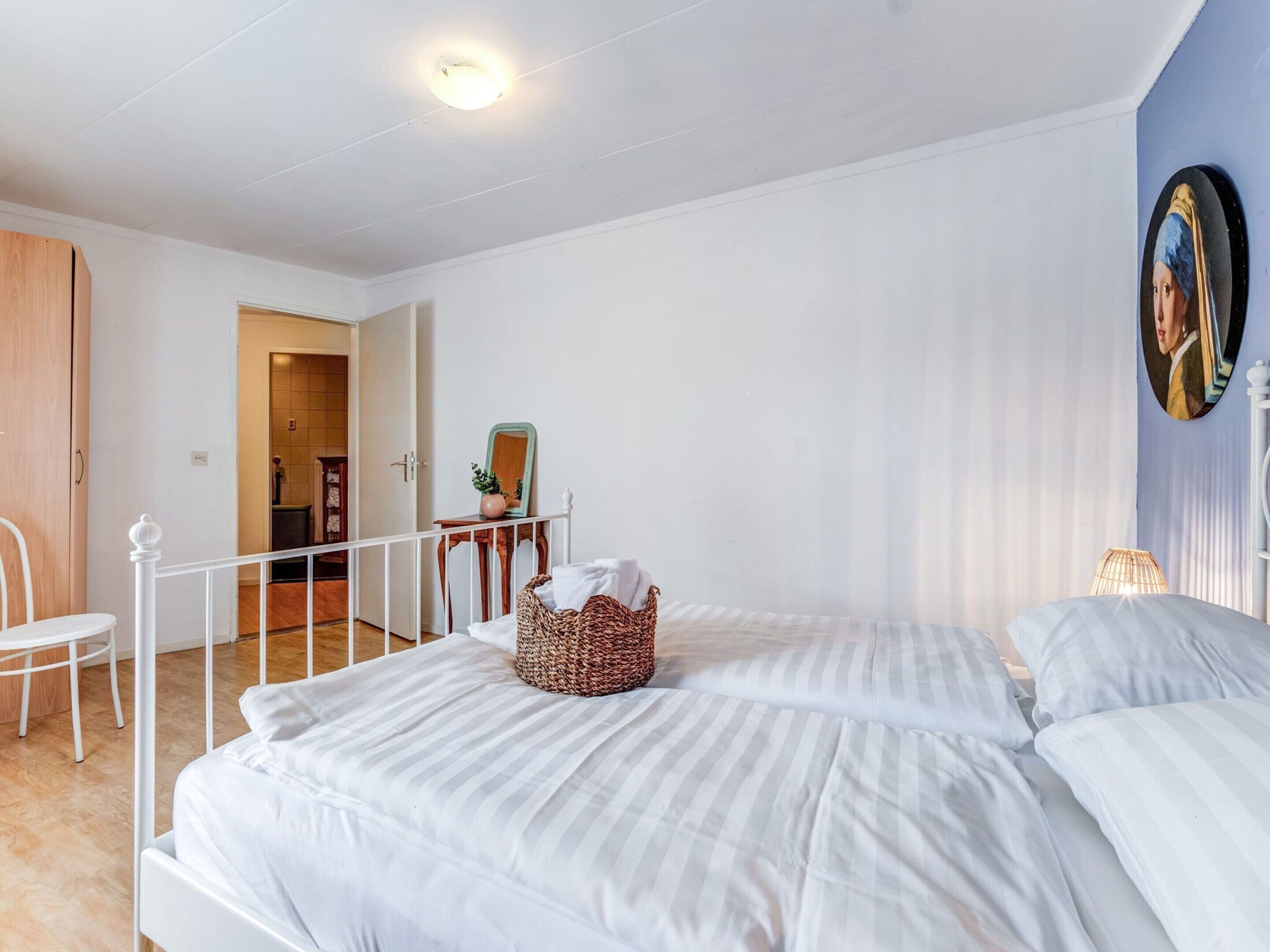 Quarto com uma cama grande, uma cadeira, uma mesinha de cabeceira com um espelho e um quadro pendurado na parede.