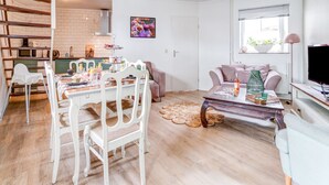 Ein gemütliches Wohnzimmer mit Essbereich, einer Küche im Hintergrund, einer Couch, einem Couchtisch und einem Fernseher.