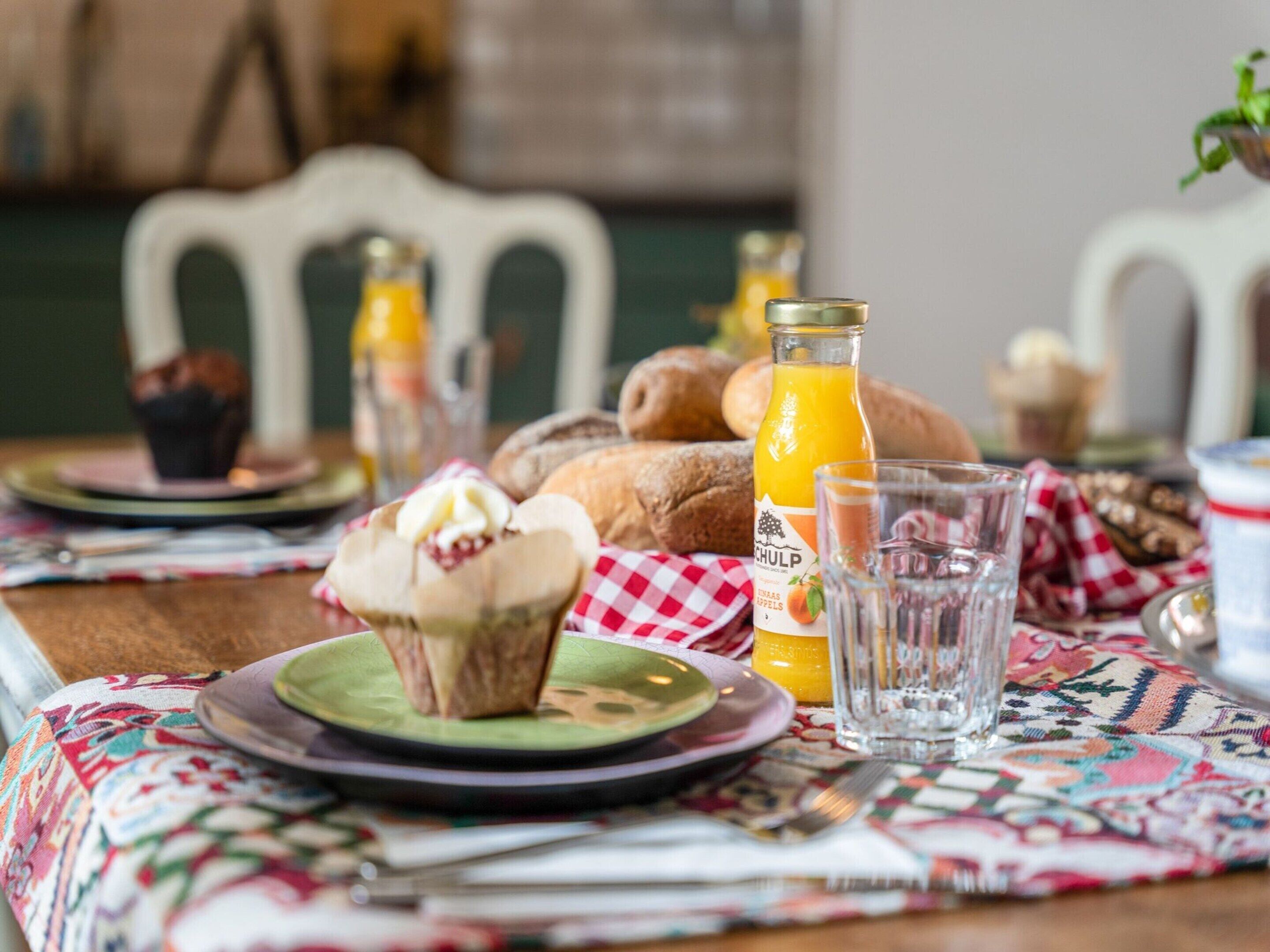 A breakfast setting with a muffin, croissant, orange juice, and a bottle of juice on a table with a checkered tablecloth.