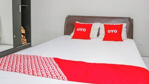A hotel room with a bed, two red pillows with the word "OYO" on them, a white and red blanket, and a door with a view of a balcony. - OYO 94117 Mr Rooms Appartement Mutiara (Bekasi)