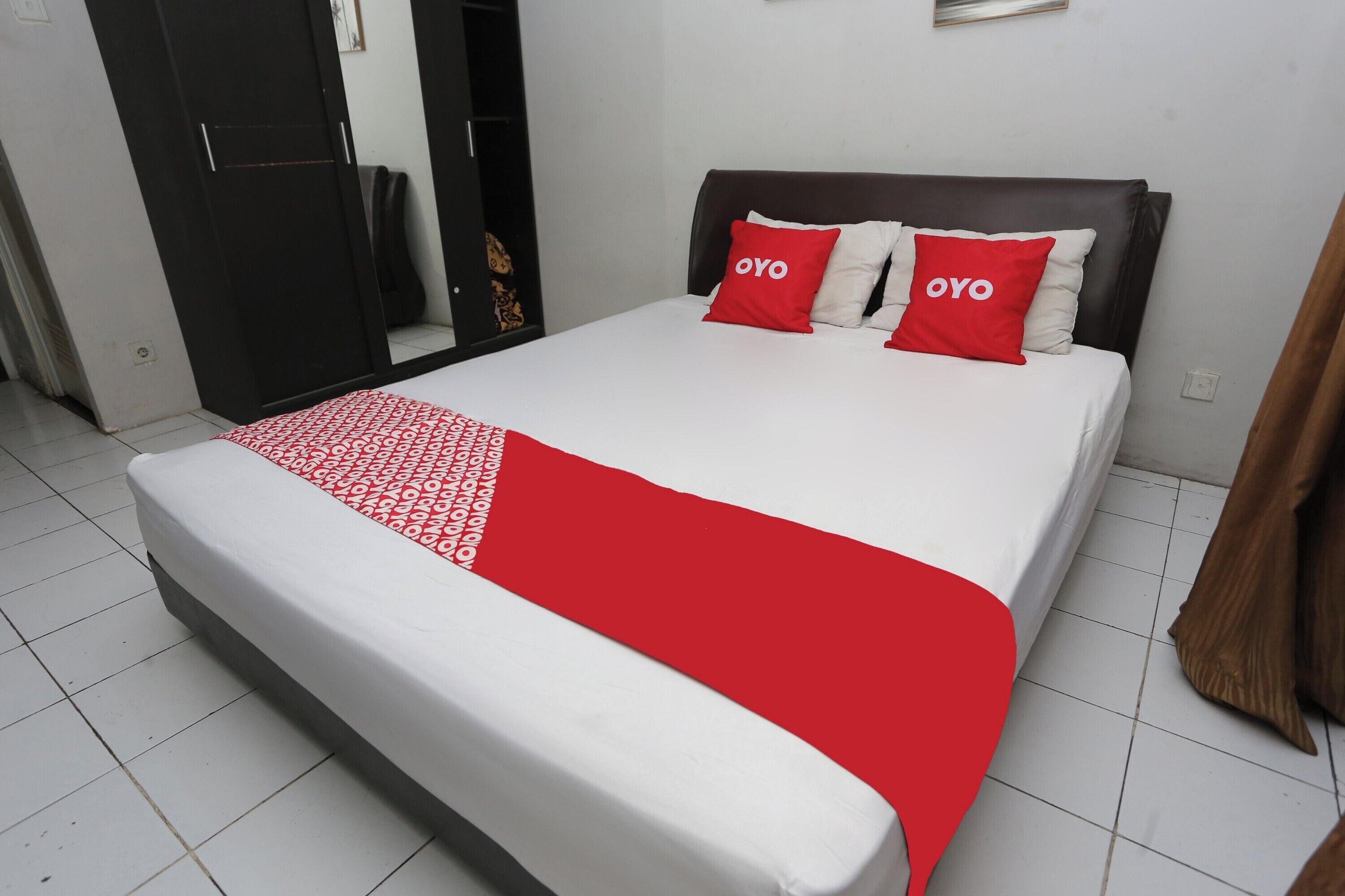 Une chambre d’hôtel avec un lit, deux oreillers rouges ornés du texte « OYO », une couverture blanche et rouge à motifs et une tête de lit sombre.