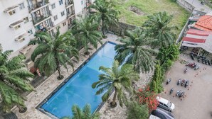 A rooftop pool surrounded by palm trees, adjacent to a multi-story building with balconies. - OYO 94117 Mr Rooms Appartement Mutiara (Bekasi)