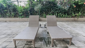 Two wicker lounge chairs with metal frames on a tiled patio, surrounded by lush greenery. - OYO 94117 Mr Rooms Appartement Mutiara (Bekasi)