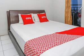 A bed with a white and red patterned bedspread, two red pillows with "OYO" text, and a brown headboard. - OYO 94117 Mr Rooms Appartement Mutiara (Bekasi)