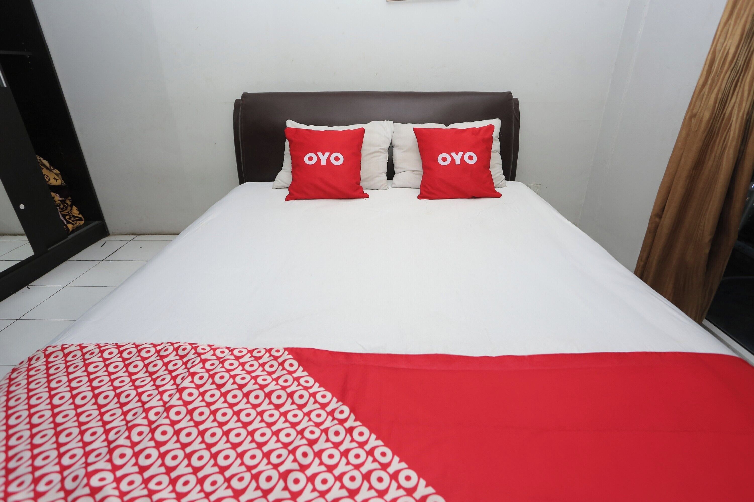 A bed with two red pillows, a white and red blanket, and a brown headboard.