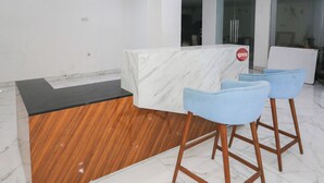 A reception desk with a marble top, a wooden counter, and two blue bar stools. - OYO 94117 Mr Rooms Appartement Mutiara (Bekasi)