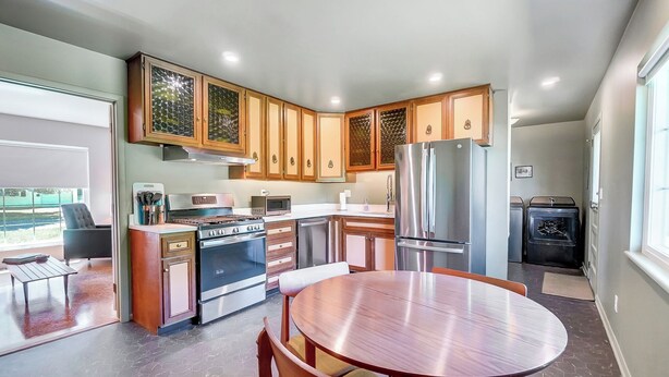 A modern kitchen with wooden cabinets, stainless steel appliances, and a round dining table. - Retro Refuge On Woodstock Dr. (Van Wert)