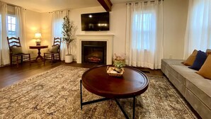 Sala de estar com lareira, televisão montada acima e mesa de centro redonda, além de sofá com almofadas.
