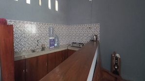 A kitchen with a long wooden countertop, a tiled backsplash, and a window above the sink. - Hotel O Homestay Gua Pindul Kang Haris (Karangmojo)