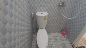 A small, tiled bathroom with a white toilet, a shower area, and a pink cleaning brush. - Hotel O Homestay Gua Pindul Kang Haris (Karangmojo)