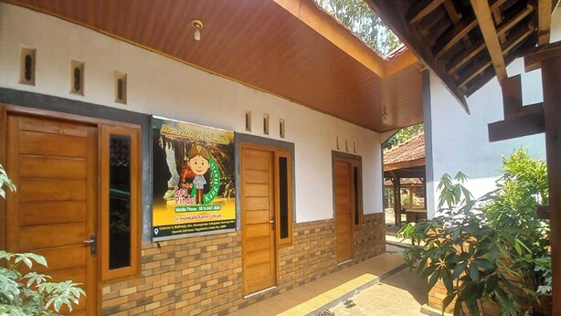 A building with a brick facade, wooden doors, and a covered walkway. - Hotel O Homestay Gua Pindul Kang Haris (Karangmojo)